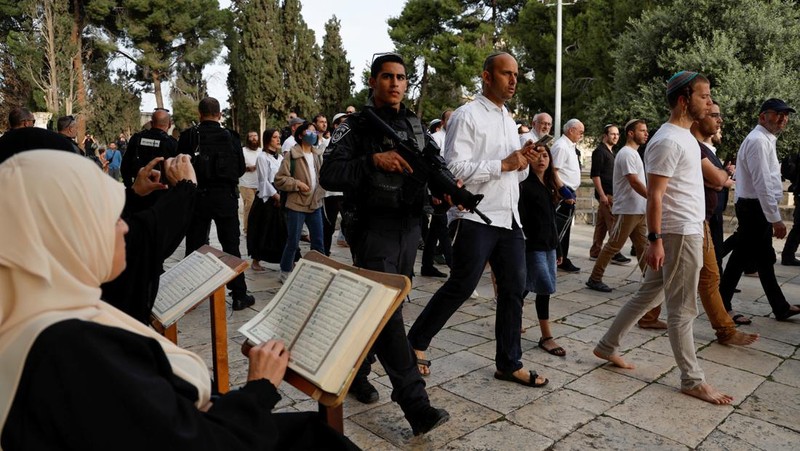 Pengunjung Yahudi berjalan melewati orang-orang yang membaca Alquran, di kompleks Masjid Al-Aqsa, yang dikenal umat Islam sebagai Tempat Suci Mulia dan bagi orang Yahudi sebagai Temple Mount, sementara ketegangan muncul selama bentrokan di Kota Tua Yerusalem, 9 April 2023. (REUTERS/Ammar Awad)