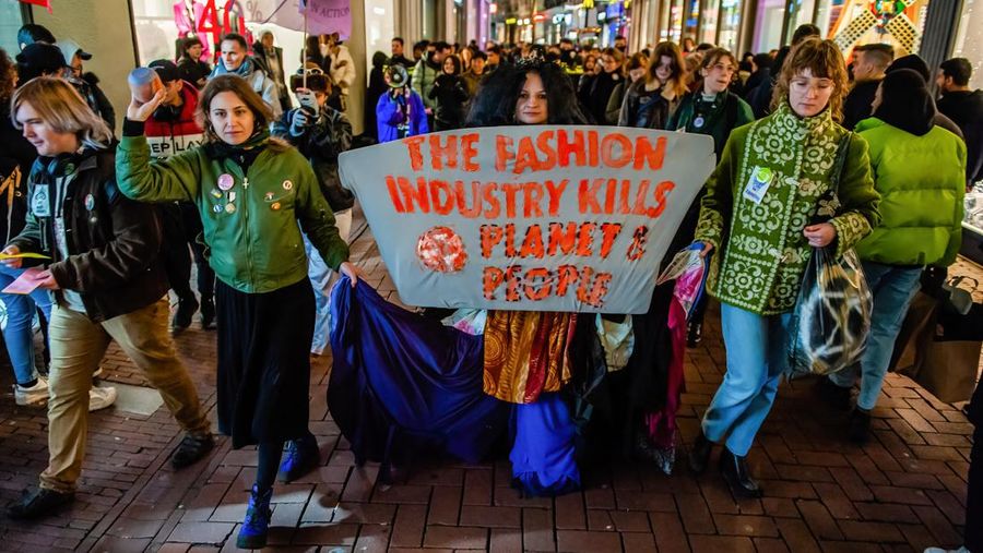 AMSTERDAM, NETHERLANDS - 2022/11/25: An XR activist marches with a banner against the fashion industry during the Black Friday Extinction Rebellion demonstration. The Extinction Rebellion (XR) climate organization organized a demonstration against overconsumption during Black Friday. The activists carried out an action called Free (ky) Friday at the Dam Square, where they placed hundreds of second-hand clothes that people could take for free or swap clothes. With this action, the organization wants to put profit above people and the planet and break with the Consumer culture. According to XR, the fashion industry is responsible for between 3 and 10 percent of global greenhouse gas emissions. Even though the industry is a promising improvement, 96% of big brands still need to be clear about their product chains and the wages they pay their workers. (Photo by Ana Fernandez/SOPA Images/LightRocket via Getty Images)