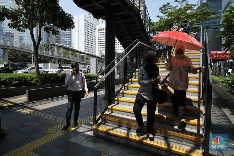 Warga menggunakan payung untuk menghindari paparan sinar matahari di kawasan Jakarta, Senin (17/4/2023). (CNBC Indonesia/Tri Susilo)