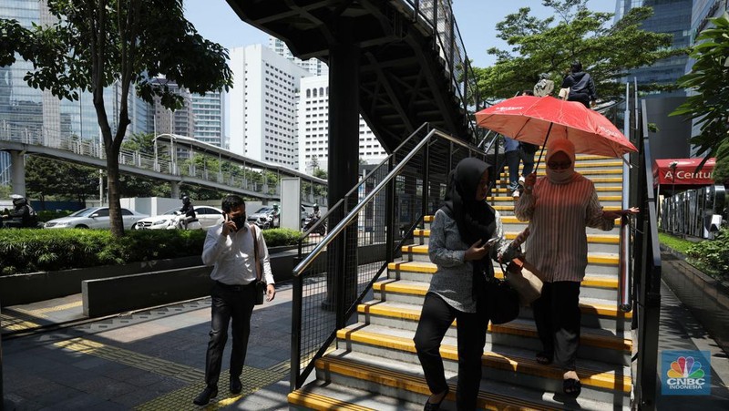 Warga menggunakan payung untuk menghindari paparan sinar matahari di kawasan Jakarta, Senin (17/4/2023). (CNBC Indonesia/Tri Susilo)