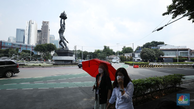Warga menggunakan payung untuk menghindari paparan sinar matahari di kawasan Jakarta, Senin (17/4/2023). (CNBC Indonesia/Tri Susilo)