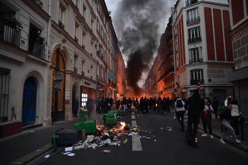 Para pengunjuk rasa berkumpul ketika seorang demonstran memegang topeng yang menggambarkan Presiden Prancis Emmanuel Macron dan berpakaian seperti seorang raja, selama demonstrasi menyusul pidato khusus kepada negara oleh Macron, setelah dia menandatangani undang-undang reformasi pensiun yang menaikkan usia pensiun, di Paris, Prancis, 17 April 2023. (REUTERS/Stephanie Lecocq)