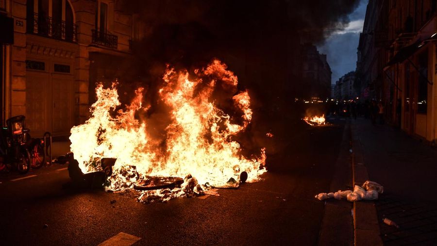 Para pengunjuk rasa berkumpul ketika seorang demonstran memegang topeng yang menggambarkan Presiden Prancis Emmanuel Macron dan berpakaian seperti seorang raja, selama demonstrasi menyusul pidato khusus kepada negara oleh Macron, setelah dia menandatangani undang-undang reformasi pensiun yang menaikkan usia pensiun, di Paris, Prancis, 17 April 2023. (REUTERS/Stephanie Lecocq)