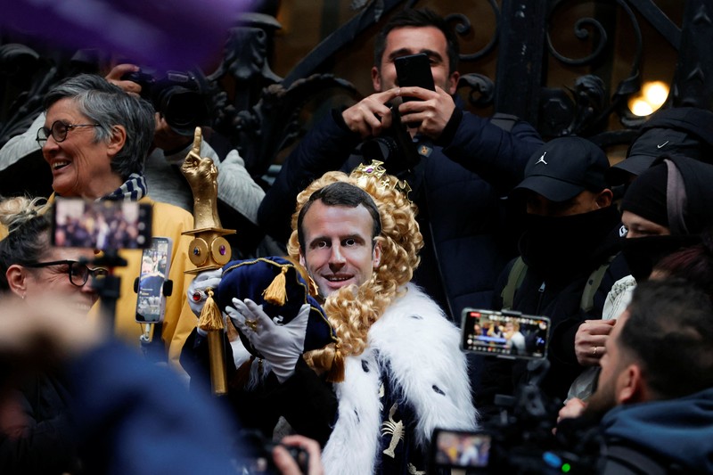 Para pengunjuk rasa berkumpul ketika seorang demonstran memegang topeng yang menggambarkan Presiden Prancis Emmanuel Macron dan berpakaian seperti seorang raja, selama demonstrasi menyusul pidato khusus kepada negara oleh Macron, setelah dia menandatangani undang-undang reformasi pensiun yang menaikkan usia pensiun, di Paris, Prancis, 17 April 2023. Para pengunjuk rasa berkumpul ketika seorang demonstran memegang topeng yang menggambarkan Presiden Prancis Emmanuel Macron dan berpakaian seperti seorang raja, selama demonstrasi menyusul pidato khusus kepada negara oleh Macron, setelah dia menandatangani undang-undang reformasi pensiun yang menaikkan usia pensiun, di Paris, Prancis, 17 April 2023. (REUTERS/Stephanie Lecocq)