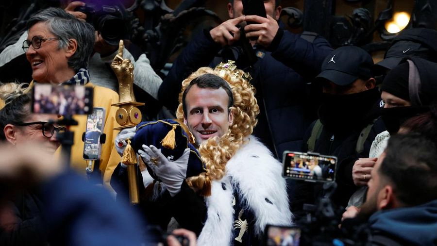 Para pengunjuk rasa berkumpul ketika seorang demonstran memegang topeng yang menggambarkan Presiden Prancis Emmanuel Macron dan berpakaian seperti seorang raja, selama demonstrasi menyusul pidato khusus kepada negara oleh Macron, setelah dia menandatangani undang-undang reformasi pensiun yang menaikkan usia pensiun, di Paris, Prancis, 17 April 2023. (REUTERS/Stephanie Lecocq)