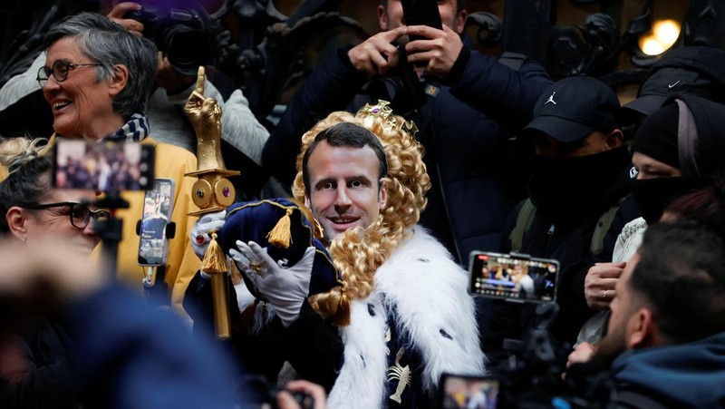 Para pengunjuk rasa berkumpul ketika seorang demonstran memegang topeng yang menggambarkan Presiden Prancis Emmanuel Macron dan berpakaian seperti seorang raja, selama demonstrasi menyusul pidato khusus kepada negara oleh Macron, setelah dia menandatangani undang-undang reformasi pensiun yang menaikkan usia pensiun, di Paris, Prancis, 17 April 2023. (REUTERS/Stephanie Lecocq)