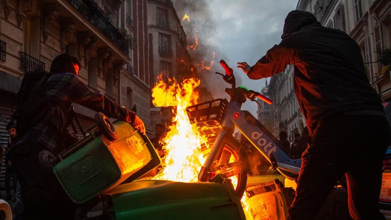Para pengunjuk rasa berkumpul ketika seorang demonstran memegang topeng yang menggambarkan Presiden Prancis Emmanuel Macron dan berpakaian seperti seorang raja, selama demonstrasi menyusul pidato khusus kepada negara oleh Macron, setelah dia menandatangani undang-undang reformasi pensiun yang menaikkan usia pensiun, di Paris, Prancis, 17 April 2023. (REUTERS/Stephanie Lecocq)