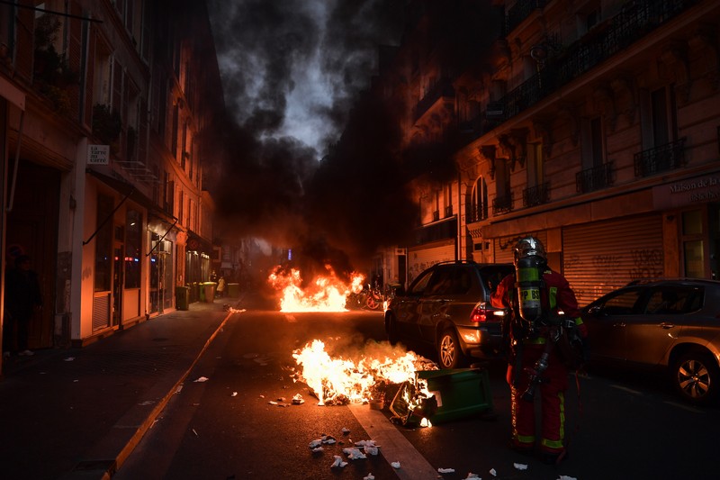 Para pengunjuk rasa berkumpul ketika seorang demonstran memegang topeng yang menggambarkan Presiden Prancis Emmanuel Macron dan berpakaian seperti seorang raja, selama demonstrasi menyusul pidato khusus kepada negara oleh Macron, setelah dia menandatangani undang-undang reformasi pensiun yang menaikkan usia pensiun, di Paris, Prancis, 17 April 2023. (REUTERS/Stephanie Lecocq)