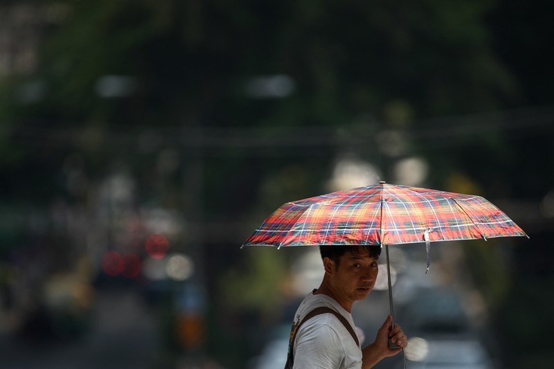 Orang-orang memegang payung saat menyeberang jalan saat suhu mencapai rekor 45,4 derajat Celcius (113,7 Fahrenheit) di Bangkok, Thailand, 22 April 2023. (REUTERS/Chalinee Thirasupa)