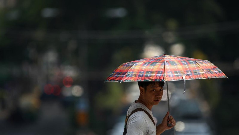 Orang-orang memegang payung saat menyeberang jalan saat suhu mencapai rekor 45,4 derajat Celcius (113,7 Fahrenheit) di Bangkok, Thailand, 22 April 2023. (REUTERS/Chalinee Thirasupa)