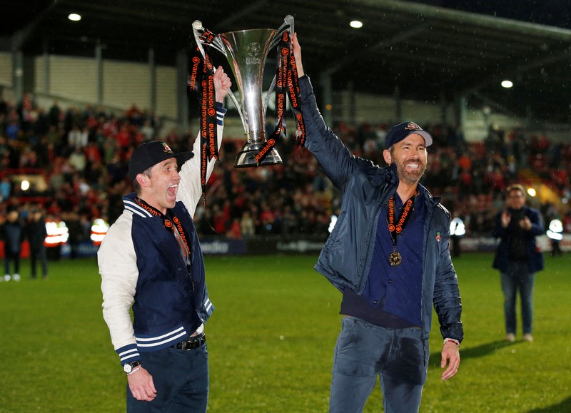 Soccer Football - National League - Wrexham v Boreham Wood - Racecourse Ground, Wrexham, Britain - April 22, 2023 Wrexham co-owners Rob McElhenney and Ryan Reynolds celebrate with the trophy on the pitch after Wrexham win the National League and promotion to League Two Action Images via Reuters/Ed Sykes EDITORIAL USE ONLY. No use with unauthorized audio, video, data, fixture lists, club/league logos or 'live' services. Online in-match use limited to 75 images, no video emulation. No use in betting, games or single club /league/player publications.  Please contact your account representative for further details.     TPX IMAGES OF THE DAY