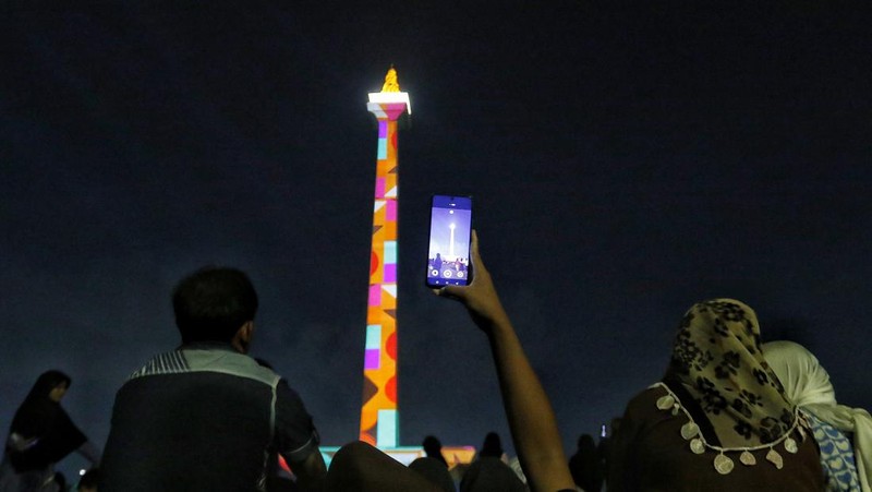 Pengunjung menyaksikan tayangan video mapping di kawasan Monas Jakarta Indonesia pada 23 April 2023. Bertepatan dengan libur Idul Fitri, Pemprov DKI Jakarta menggelar Pekan Kegiatan Monas 2023 yang ditandai dengan tayangan video mapping. (Eko Siswono Toyudho/Anadolu Agency via Getty Images)