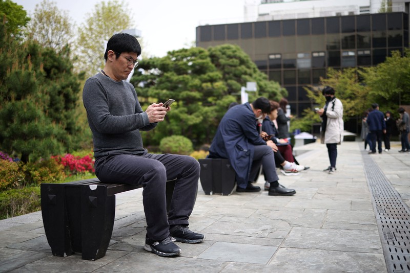 SOUTHKOREA-APPS/ECONOMY Office workers look at their mobile phones to check the local online banking app Toss as they gather at Seoul Museum of Art during a lunch break in Seoul, South Korea, April 13, 2023. REUTERS/Kim Hong-Ji