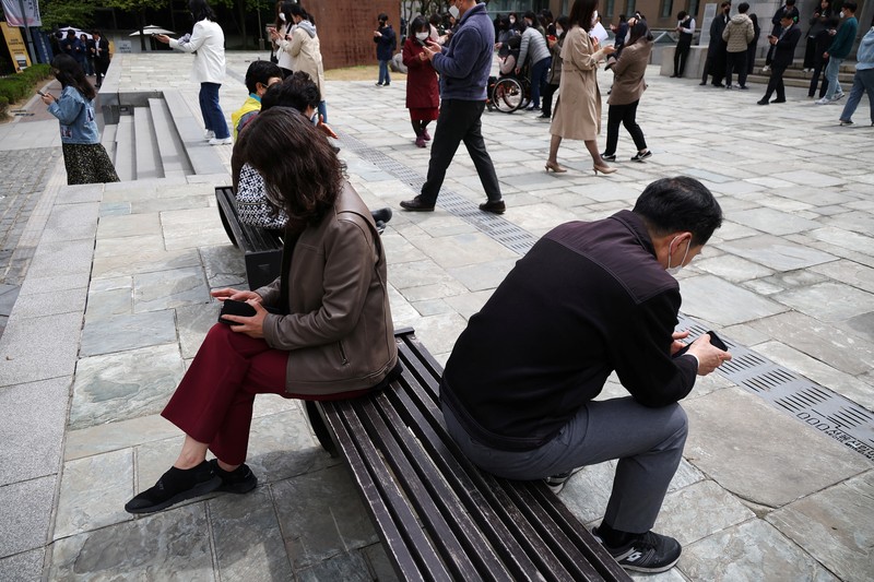SOUTHKOREA-APPS/ECONOMY Office workers look at their mobile phones to check the local online banking app Toss as they gather at Seoul Museum of Art during a lunch break in Seoul, South Korea, April 13, 2023. REUTERS/Kim Hong-Ji