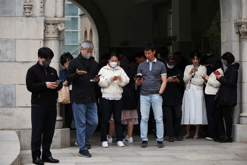 SOUTHKOREA-APPS/ECONOMY Office workers look at their mobile phones to check the local online banking app Toss as they gather at Seoul Museum of Art during a lunch break in Seoul, South Korea, April 13, 2023. REUTERS/Kim Hong-Ji