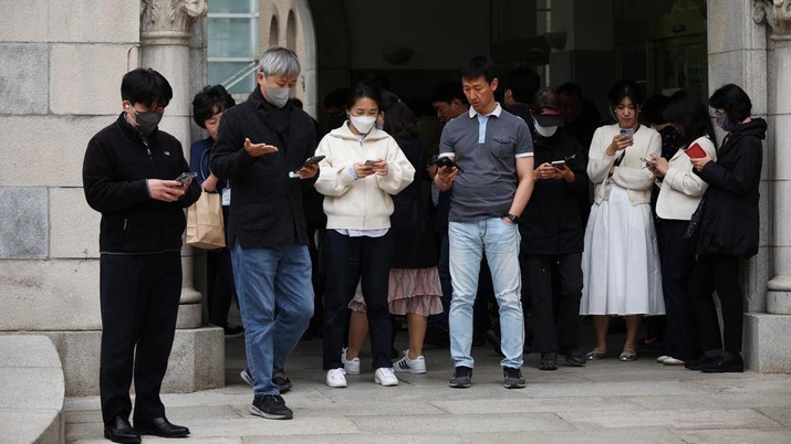 Office workers look at their mobile phones to check the local online banking app Toss as they gather at Seoul Museum of Art during a lunch break in Seoul, South Korea, April 13, 2023.  REUTERS/Kim Hong-Ji