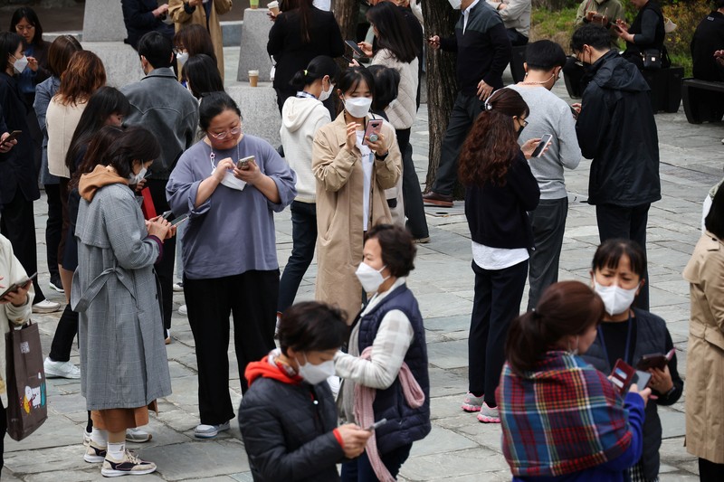 SOUTHKOREA-APPS/ECONOMY Office workers look at their mobile phones to check the local online banking app Toss as they gather at Seoul Museum of Art during a lunch break in Seoul, South Korea, April 13, 2023. REUTERS/Kim Hong-Ji