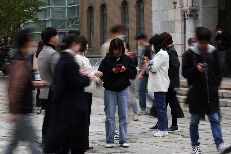 SOUTHKOREA-APPS/ECONOMY Office workers look at their mobile phones to check the local online banking app Toss as they gather at Seoul Museum of Art during a lunch break in Seoul, South Korea, April 13, 2023. REUTERS/Kim Hong-Ji