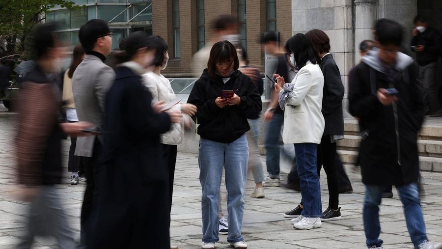 Office workers look at their mobile phones to check the local online banking app Toss as they gather at Seoul Museum of Art during a lunch break in Seoul, South Korea, April 13, 2023. REUTERS/Kim Hong-Ji