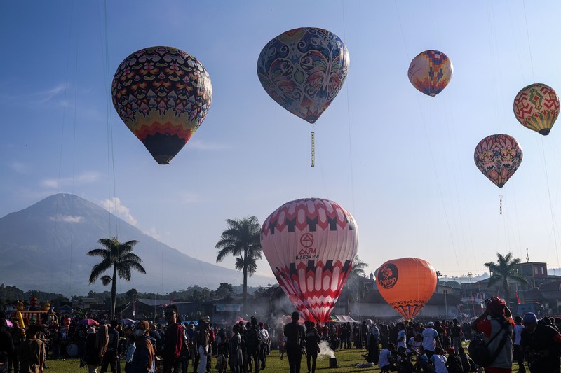1252105442 WONOSOBO, INDONESIA - APRIL 23: Hot air balloons fly over the sky during a balloon festival on the Eid al-Fitr holiday at Ronggolawe Stadion on April 23, 2023, in Wonosobo, Central Java, Indonesia. Javanese people fly giant hot air balloons during Eid, which has long been a tradition of the Wonosobo regency. (Photo by Garry Lotulung/Anadolu Agency via Getty Images)