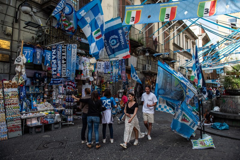 Bendera, spanduk, dan pita dipajang di jalan-jalan untuk merayakan kemenangan gelar Serie A ketiga pada 27 April 2023 di Naples, Italia. Kota Naples sedang bersiap untuk merayakan kemenangan Scudetto ketiga di kejuaraan Serie A. Di jalan-jalan pusat bersejarah dan di berbagai distrik Napoli, dekorasi, bendera, dan spanduk telah dipasang untuk merayakan kejuaraan sepak bola yang dimainkan oleh tim yang dilatih oleh Spalletti. Para pemain bisa menjadi juara Italia lebih awal, jika mereka berhasil mengalahkan Salernitana dalam derby Campania dalam pertandingan yang akan dimainkan pada hari Minggu pukul 15:00 di Stadion Diego Armando Maradona dan jika Lazio gagal menang tandang melawan Internazionale. Napoli telah memenangkan dua Scudetti dalam sejarahnya pada musim 1986-1987 dan 1989-1990, kedua kemenangan tersebut diperoleh dengan kehadiran Diego Armando Maradona, para fans Neapolitan menunggu untuk dapat merayakan 33 tahun setelah kesuksesan terakhir. (Ivan Romano/Getty Images)