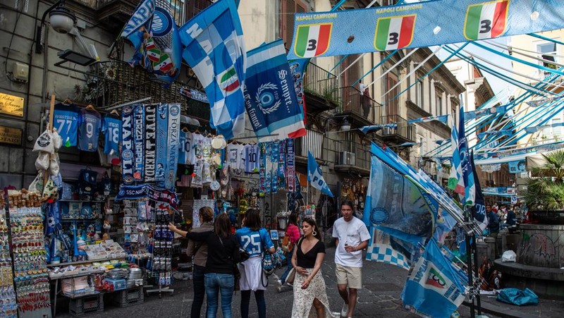 Bendera, spanduk, dan pita dipajang di jalan-jalan untuk merayakan kemenangan gelar Serie A ketiga pada 27 April 2023 di Naples, Italia. Kota Naples sedang bersiap untuk merayakan kemenangan Scudetto ketiga di kejuaraan Serie A. Di jalan-jalan pusat bersejarah dan di berbagai distrik Napoli, dekorasi, bendera, dan spanduk telah dipasang untuk merayakan kejuaraan sepak bola yang dimainkan oleh tim yang dilatih oleh Spalletti. Para pemain bisa menjadi juara Italia lebih awal, jika mereka berhasil mengalahkan Salernitana dalam derby Campania dalam pertandingan yang akan dimainkan pada hari Minggu pukul 15:00 di Stadion Diego Armando Maradona dan jika Lazio gagal menang tandang melawan Internazionale. Napoli telah memenangkan dua Scudetti dalam sejarahnya pada musim 1986-1987 dan 1989-1990, kedua kemenangan tersebut diperoleh dengan kehadiran Diego Armando Maradona, para fans Neapolitan menunggu untuk dapat merayakan 33 tahun setelah kesuksesan terakhir. (Ivan Romano/Getty Images)