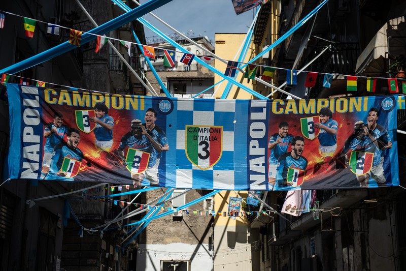 Bendera, spanduk, dan pita dipajang di jalan-jalan untuk merayakan kemenangan gelar Serie A ketiga pada 27 April 2023 di Naples, Italia. Kota Naples sedang bersiap untuk merayakan kemenangan Scudetto ketiga di kejuaraan Serie A. Di jalan-jalan pusat bersejarah dan di berbagai distrik Napoli, dekorasi, bendera, dan spanduk telah dipasang untuk merayakan kejuaraan sepak bola yang dimainkan oleh tim yang dilatih oleh Spalletti. Para pemain bisa menjadi juara Italia lebih awal, jika mereka berhasil mengalahkan Salernitana dalam derby Campania dalam pertandingan yang akan dimainkan pada hari Minggu pukul 15:00 di Stadion Diego Armando Maradona dan jika Lazio gagal menang tandang melawan Internazionale. Napoli telah memenangkan dua Scudetti dalam sejarahnya pada musim 1986-1987 dan 1989-1990, kedua kemenangan tersebut diperoleh dengan kehadiran Diego Armando Maradona, para fans Neapolitan menunggu untuk dapat merayakan 33 tahun setelah kesuksesan terakhir. (Ivan Romano/Getty Images)