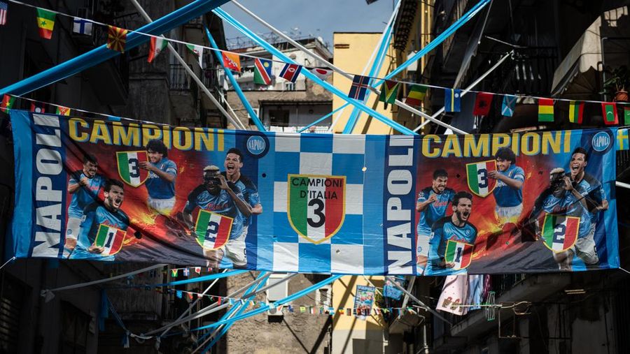 Bendera, spanduk, dan pita dipajang di jalan-jalan untuk merayakan kemenangan gelar Serie A ketiga pada 27 April 2023 di Naples, Italia. Kota Naples sedang bersiap untuk merayakan kemenangan Scudetto ketiga di kejuaraan Serie A. Di jalan-jalan pusat bersejarah dan di berbagai distrik Napoli, dekorasi, bendera, dan spanduk telah dipasang untuk merayakan kejuaraan sepak bola yang dimainkan oleh tim yang dilatih oleh Spalletti. Para pemain bisa menjadi juara Italia lebih awal, jika mereka berhasil mengalahkan Salernitana dalam derby Campania dalam pertandingan yang akan dimainkan pada hari Minggu pukul 15:00 di Stadion Diego Armando Maradona dan jika Lazio gagal menang tandang melawan Internazionale. Napoli telah memenangkan dua Scudetti dalam sejarahnya pada musim 1986-1987 dan 1989-1990, kedua kemenangan tersebut diperoleh dengan kehadiran Diego Armando Maradona, para fans Neapolitan menunggu untuk dapat merayakan 33 tahun setelah kesuksesan terakhir. (Ivan Romano/Getty Images)