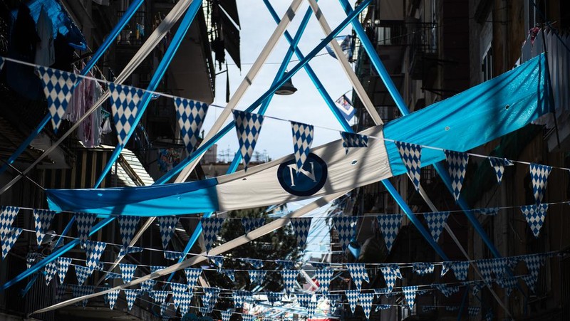 Bendera, spanduk, dan pita dipajang di jalan-jalan untuk merayakan kemenangan gelar Serie A ketiga pada 27 April 2023 di Naples, Italia. Kota Naples sedang bersiap untuk merayakan kemenangan Scudetto ketiga di kejuaraan Serie A. Di jalan-jalan pusat bersejarah dan di berbagai distrik Napoli, dekorasi, bendera, dan spanduk telah dipasang untuk merayakan kejuaraan sepak bola yang dimainkan oleh tim yang dilatih oleh Spalletti. Para pemain bisa menjadi juara Italia lebih awal, jika mereka berhasil mengalahkan Salernitana dalam derby Campania dalam pertandingan yang akan dimainkan pada hari Minggu pukul 15:00 di Stadion Diego Armando Maradona dan jika Lazio gagal menang tandang melawan Internazionale. Napoli telah memenangkan dua Scudetti dalam sejarahnya pada musim 1986-1987 dan 1989-1990, kedua kemenangan tersebut diperoleh dengan kehadiran Diego Armando Maradona, para fans Neapolitan menunggu untuk dapat merayakan 33 tahun setelah kesuksesan terakhir. (Ivan Romano/Getty Images)