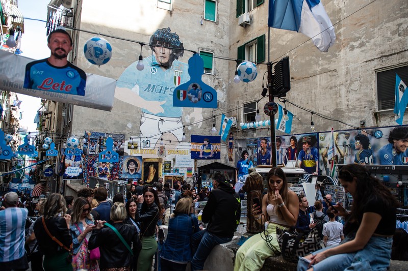 Bendera, spanduk, dan pita dipajang di jalan-jalan untuk merayakan kemenangan gelar Serie A ketiga pada 27 April 2023 di Naples, Italia. Bendera, spanduk, dan pita dipajang di jalan-jalan untuk merayakan kemenangan gelar Serie A ketiga pada 27 April 2023 di Naples, Italia. Kota Naples sedang bersiap untuk merayakan kemenangan Scudetto ketiga di kejuaraan Serie A. Di jalan-jalan pusat bersejarah dan di berbagai distrik Napoli, dekorasi, bendera, dan spanduk telah dipasang untuk merayakan kejuaraan sepak bola yang dimainkan oleh tim yang dilatih oleh Spalletti. Para pemain bisa menjadi juara Italia lebih awal, jika mereka berhasil mengalahkan Salernitana dalam derby Campania dalam pertandingan yang akan dimainkan pada hari Minggu pukul 15:00 di Stadion Diego Armando Maradona dan jika Lazio gagal menang tandang melawan Internazionale. Napoli telah memenangkan dua Scudetti dalam sejarahnya pada musim 1986-1987 dan 1989-1990, kedua kemenangan tersebut diperoleh dengan kehadiran Diego Armando Maradona, para fans Neapolitan menunggu untuk dapat merayakan 33 tahun setelah kesuksesan terakhir. (Ivan Romano/Getty Images)