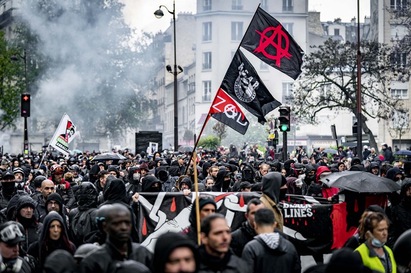French Republican Security Corps (CRS - Compagnies Republicaines de Securite) police officers and Police officers take position next to a burning bicycle-sharing station during a demonstration on May Day (Labour Day), to mark the international day of the workers, more than a month after the government pushed an unpopular pensions reform act through parliament, in Paris, on May 1, 2023. - Opposition parties and trade unions have urged protesters to maintain their three-month campaign against the law that will hike the retirement age to 64 from 62. (Photo by Geoffroy Van der Hasselt / AFP)