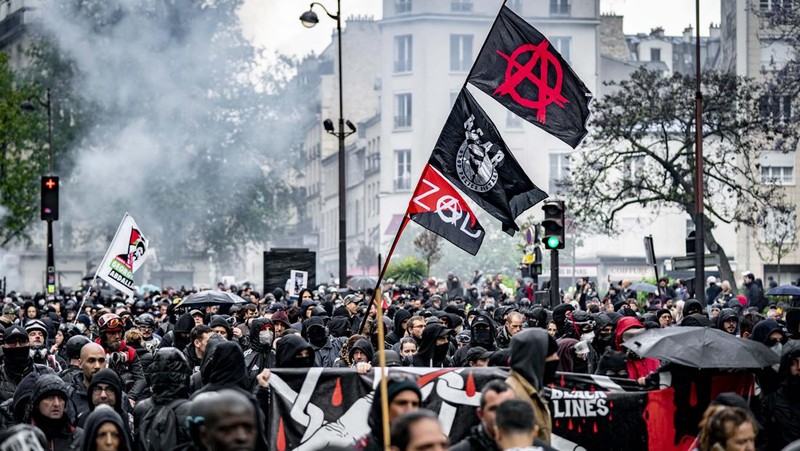 French Republican Security Corps (CRS - Compagnies Republicaines de Securite) police officers and Police officers take position next to a burning bicycle-sharing station during a demonstration on May Day (Labour Day), to mark the international day of the workers, more than a month after the government pushed an unpopular pensions reform act through parliament, in Paris, on May 1, 2023. - Opposition parties and trade unions have urged protesters to maintain their three-month campaign against the law that will hike the retirement age to 64 from 62. (Photo by Geoffroy Van der Hasselt / AFP)
