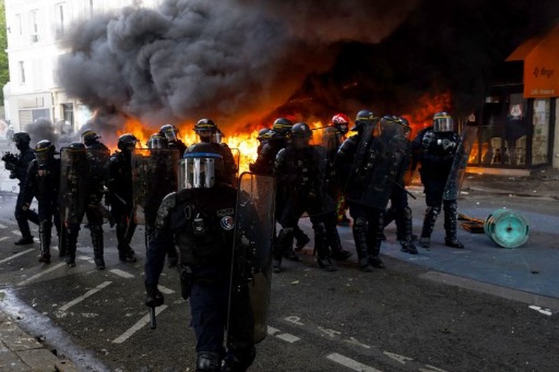 FRANCE-POLITICS-MAY-DAY-PENSIONS-DEMO French Republican Security Corps (CRS - Compagnies Republicaines de Securite) police officers and Police officers take position next to a burning bicycle-sharing station during a demonstration on May Day (Labour Day), to mark the international day of the workers, more than a month after the government pushed an unpopular pensions reform act through parliament, in Paris, on May 1, 2023. - Opposition parties and trade unions have urged protesters to maintain their three-month campaign against the law that will hike the retirement age to 64 from 62. (Photo by Geoffroy Van der Hasselt / AFP)