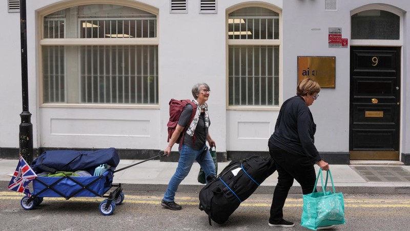 Penggemar kerajaan Inggris, Mary-Jane Willows dari Inggris dan Donna Werner dari AS berjalan ke The Mall untuk mendirikan kemah jelang Penobatan Raja Charles, di London, Inggris, Selasa (2/5/2023). REUTERS/Maja Smiejkowska