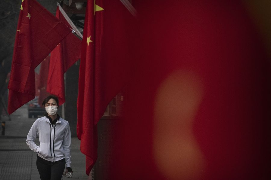 Seorang wanita mengenakan topeng pelindung saat dia berjalan di depan bendera Tiongkok di sebuah jalan selama liburan Tahun Baru Imlek dan Festival Musim Semi pada 28 Januari 2020 di Beijing, Tiongkok.