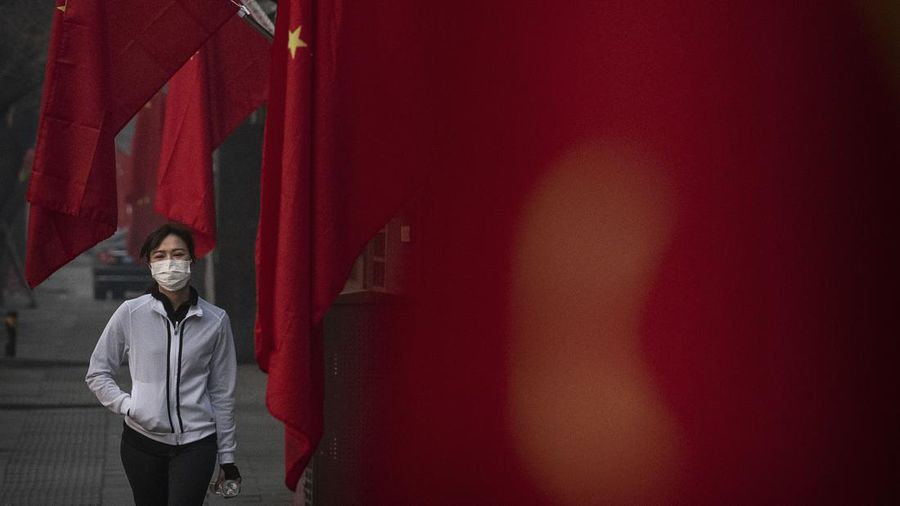 Seorang wanita mengenakan topeng pelindung saat dia berjalan di depan bendera Tiongkok di sebuah jalan selama liburan Tahun Baru Imlek dan Festival Musim Semi pada 28 Januari 2020 di Beijing, Tiongkok.  (File Foto - Kevin Frayer/Getty Images)