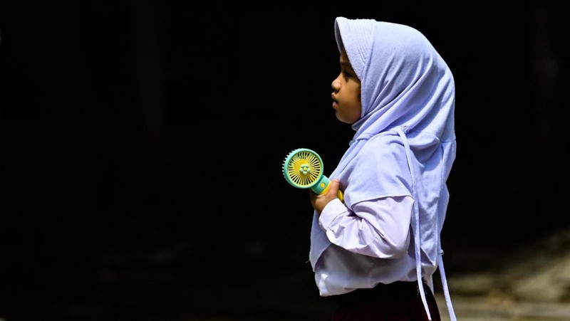 Seorang siswa sekolah dasar menggunakan kipas angin portabel untuk menjaga kesejukan saat cuaca panas di Banda Aceh pada 15 Mei 2023. (CHAIDEER MAHYUDDIN/AFP via Getty Images)