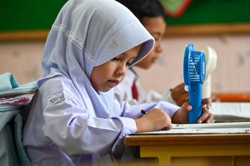 Seorang siswa sekolah dasar menggunakan kipas angin portabel untuk menjaga kesejukan saat cuaca panas di Banda Aceh pada 15 Mei 2023. (CHAIDEER MAHYUDDIN/AFP via Getty Images)