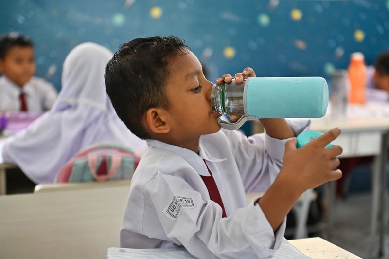 Seorang siswa sekolah dasar menggunakan kipas angin portabel untuk menjaga kesejukan saat cuaca panas di Banda Aceh pada 15 Mei 2023. (CHAIDEER MAHYUDDIN/AFP via Getty Images)