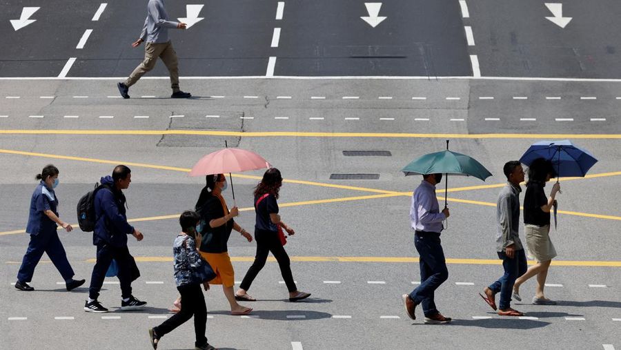 Orang-orang melindungi diri dari matahari dengan payung saat mereka menyeberang jalan pada hari yang hangat di Singapura 15 Mei 2023. (REUTERS/Edgar Su)