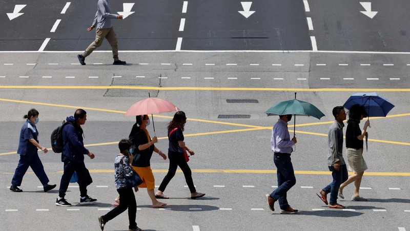 Orang-orang melindungi diri dari matahari dengan payung saat mereka menyeberang jalan pada hari yang hangat di Singapura 15 Mei 2023. (REUTERS/Edgar Su)