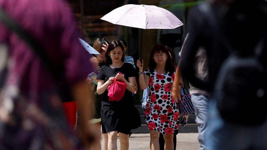 Orang-orang menggunakan payung menyeberang jalan pada hari yang hangat di Singapura 15 Mei 2023. (REUTERS/Edgar Su)
