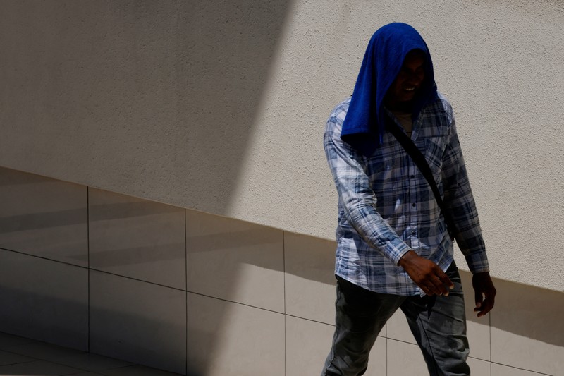 Orang-orang melindungi diri dari matahari dengan payung saat mereka menyeberang jalan pada hari yang hangat di Singapura 15 Mei 2023. (REUTERS/Edgar Su)