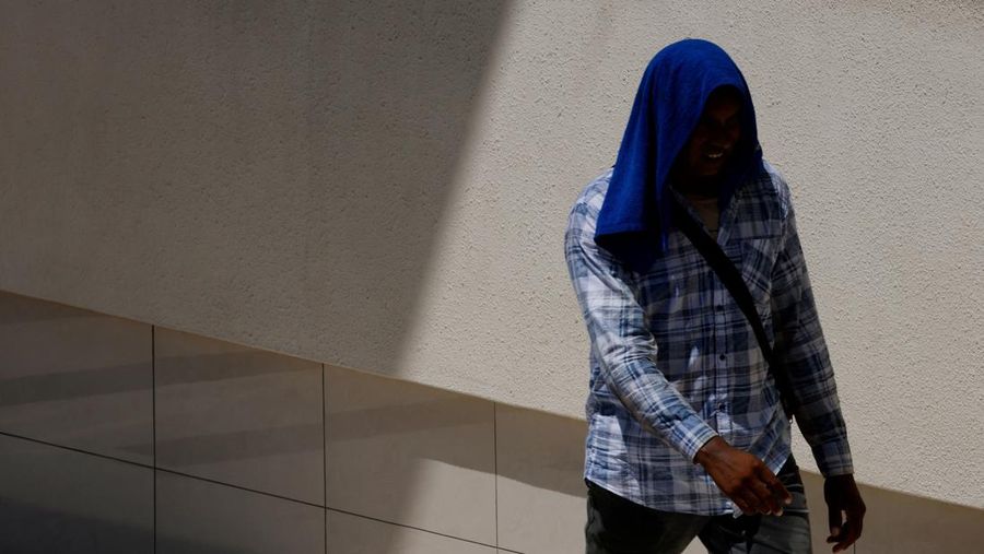 Orang-orang melindungi diri dari matahari dengan payung saat mereka menyeberang jalan pada hari yang hangat di Singapura 15 Mei 2023. (REUTERS/Edgar Su)