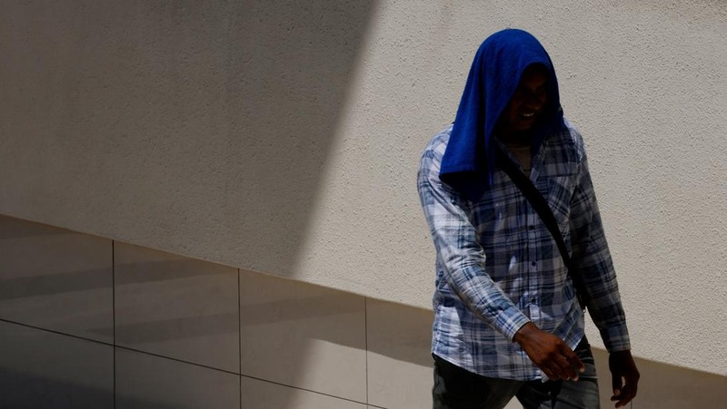Orang-orang melindungi diri dari matahari dengan payung saat mereka menyeberang jalan pada hari yang hangat di Singapura 15 Mei 2023. (REUTERS/Edgar Su)