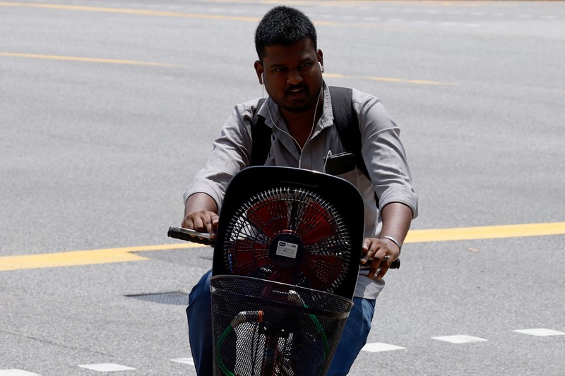 Orang-orang melindungi diri dari matahari dengan payung saat mereka menyeberang jalan pada hari yang hangat di Singapura 15 Mei 2023. (REUTERS/Edgar Su)