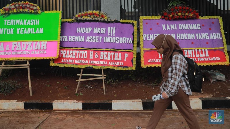 Warga melihat karangan bunga dari nasabah korban Koperasi Simpan Pinjam (KSP) Indosurya yang dipasang disepanjang jalur pedestrian kawasan kejagung, Jakarta, Rabu (24/5/2023). (CNBC Indonesia/Muhammad Sabki)