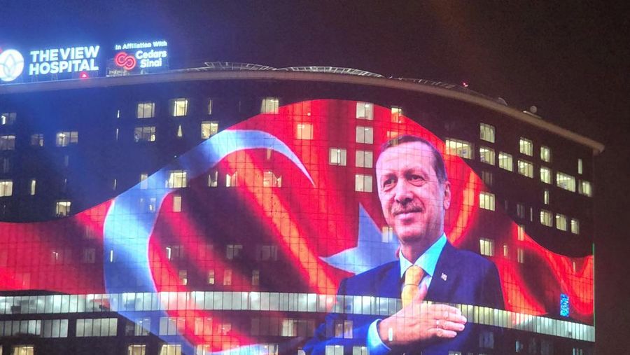 Presiden Turki Recep Tayyip Erdogan dan bendera Turki diproyeksikan di The View Hospital saat Erdogan memimpin pemilihan presiden Turki di Doha, Qatar pada 29 Mei 2023. (Ahmed Yusuf Bitmez/Anadolu Agency via Getty Images)