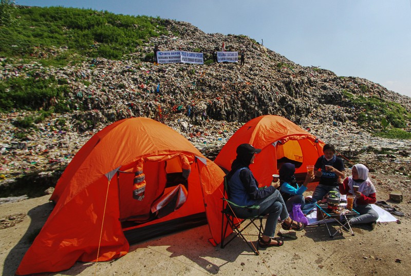 Beberapa aktivis lingkungan makan di dekat tenda mereka saat aksi damai di TPA Cipayung di Depok, Provinsi Jawa Barat Indonesia pada 31 Mei 2023. Aktivis lingkungan ambil bagian dalam aksi damai untuk menunjukkan meningkatnya penumpukan sampah yang melebihi kapasitas dan menyebabkan berbagai masalah kesehatan dan lingkungan di kota. (Eko Siswono Toyudho/Anadolu Agency via Getty Images)