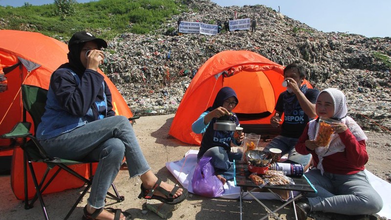 Beberapa aktivis lingkungan makan di dekat tenda mereka saat aksi damai di TPA Cipayung di Depok, Provinsi Jawa Barat Indonesia pada 31 Mei 2023. Aktivis lingkungan ambil bagian dalam aksi damai untuk menunjukkan meningkatnya penumpukan sampah yang melebihi kapasitas dan menyebabkan berbagai masalah kesehatan dan lingkungan di kota. (Eko Siswono Toyudho/Anadolu Agency via Getty Images)